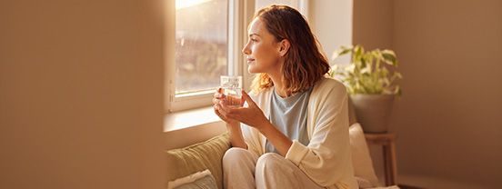 Person sitzt entspannt am Fenster mit einem Glas Wasser – Hydration gegen Stress und Reizbarkeit